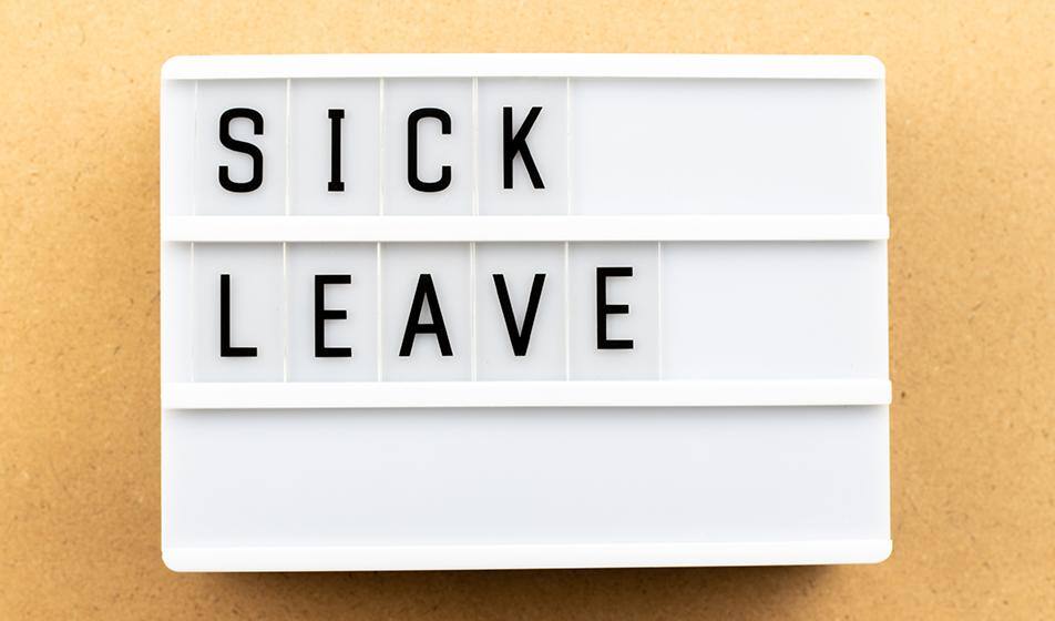 A white sign with black letters reads 'sick leave' against a golden-coloured plain background