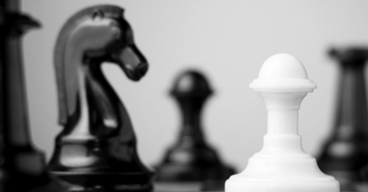 An image of black and white chess pieces. There are four black pieces and one white piece. One of the black chess pieces is a knight.