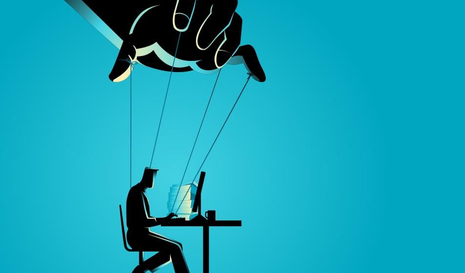 The silhouette of a man sat at a desk is shown against a blue background. A large hand hovers above him, holding strings that he is attached to, showing control and manipulation. 