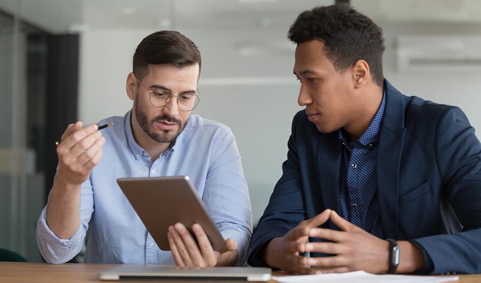 Two male colleagues are having a meeting - they are both looking at an ipad and talking calmly. 