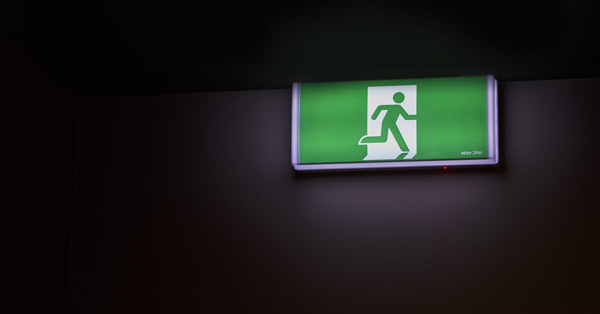 A green exit sign is hanging on a wall and lighting up a dark room.