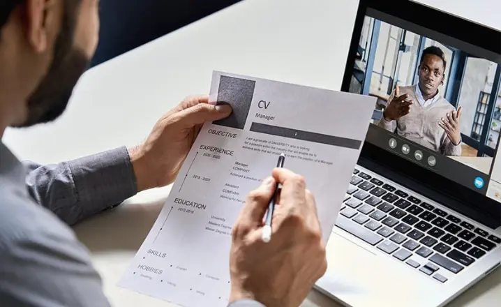 A man reviews a CV whilst the interviewee is on his laptop via video call
