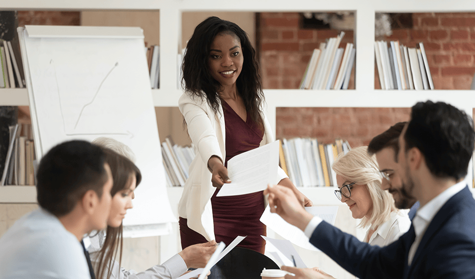 A woman hands paperwork to employees sat around a table