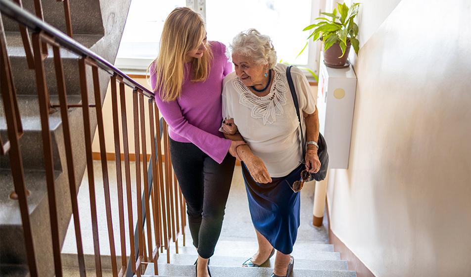 A younger woman helps an elderly woman up a flight of stairs