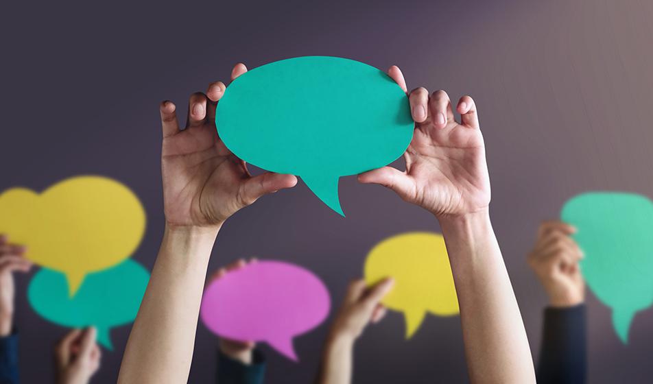 A group of people's hands are shown in the air, holding different-coloured paper speech bubbles