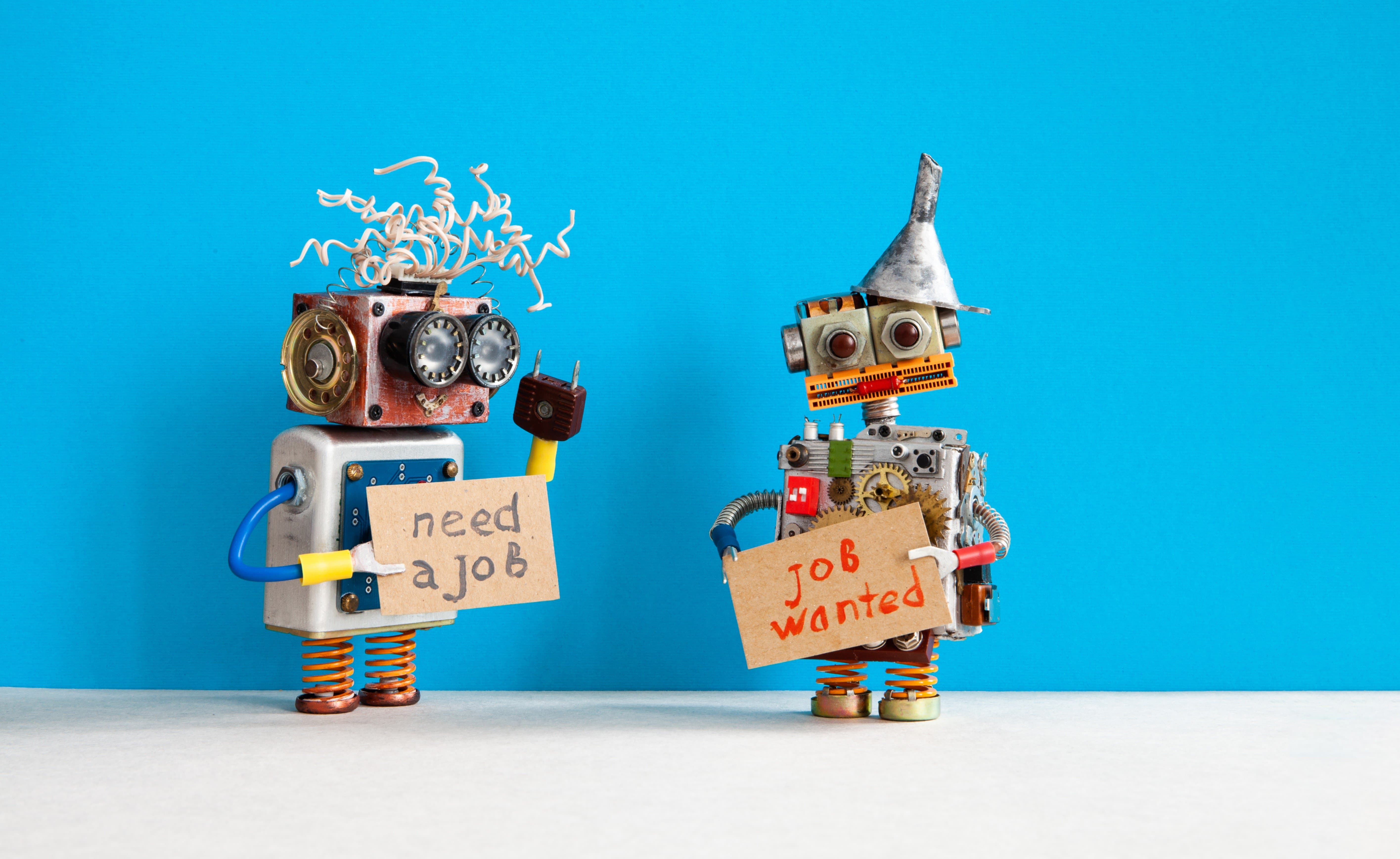 two robot figures made from household items each holding a cardboard sign asking for work