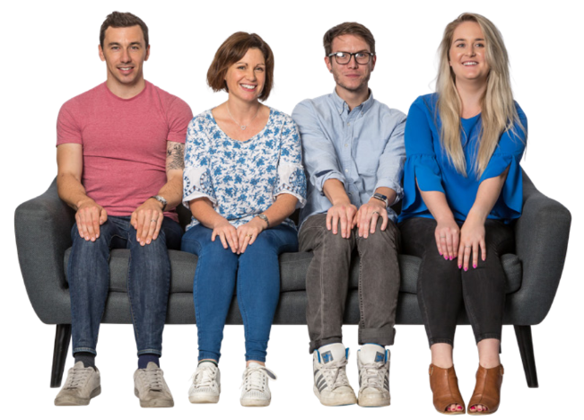 Four colleagues are sat closely together on a grey sofa. They are all smiling at the camera.