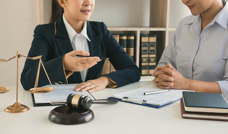 Two women having a conversation with paperwork, scales and a gavel on the table they are sat up to 