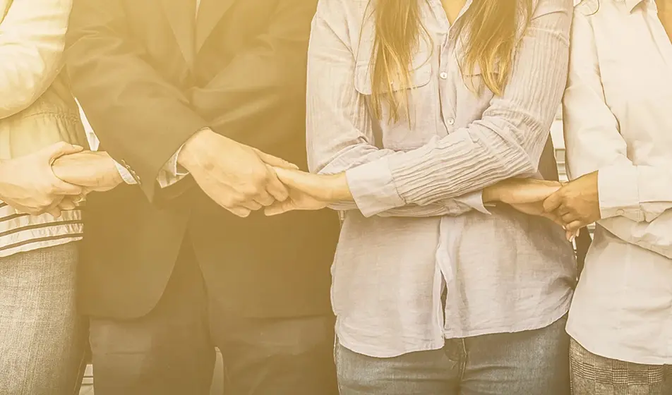 A group of people are holding hands at waist height, showing a connected team.