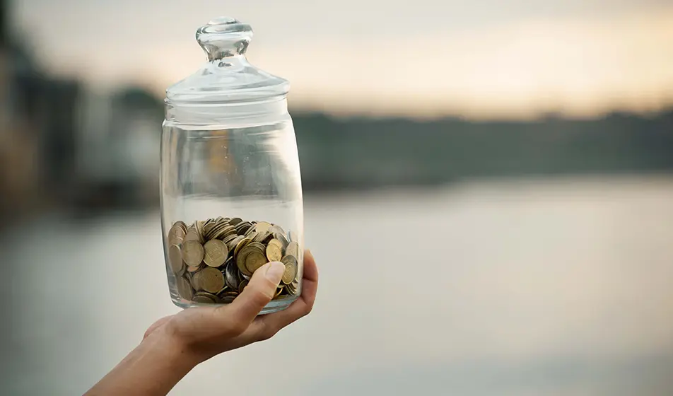A person holding a glass jar full of pennies.