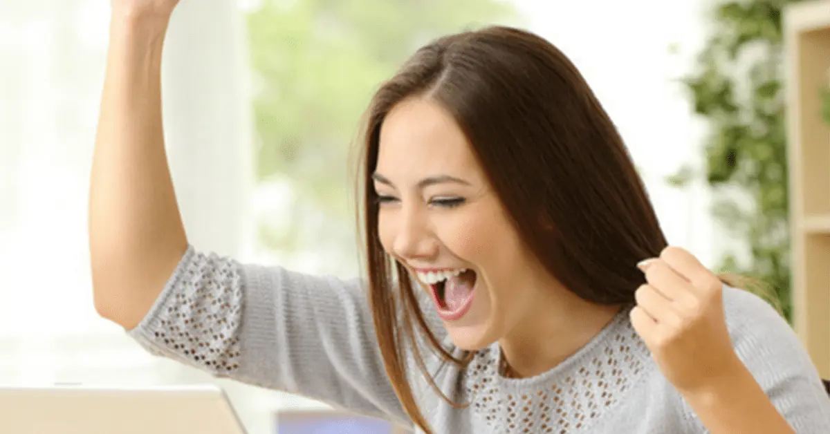 A woman is celebrating success in her personal development. She is punching a fist in the air and cheering.