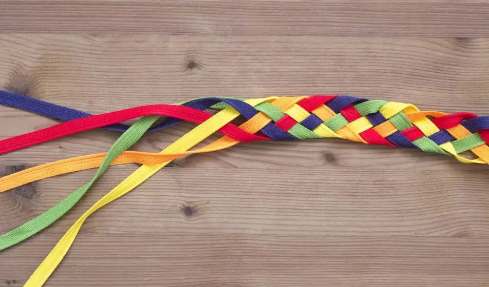 Multi-coloured ribbons have been plaited from the right of the image to the left. Some of the ribbon remains unplaited.