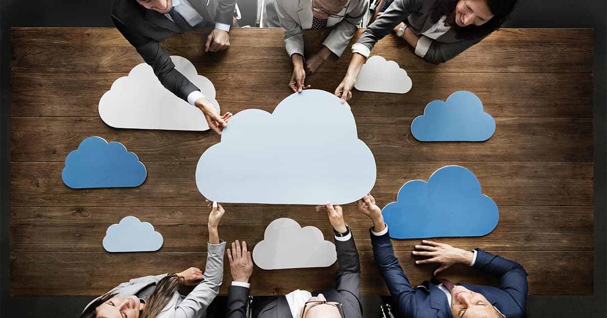 Six people are sitting around a desk and holding a large white cloud. There are several other clouds lying on the table which are blue and white.