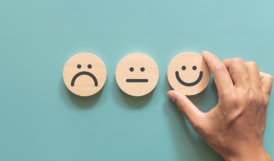 Three wooden faces are shown on wooden discs - one sad, one neutral and one happy 