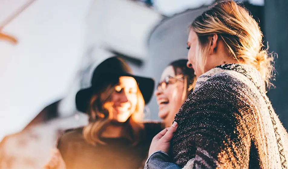 Three happy women are laughing together with the evening sun shining on them.