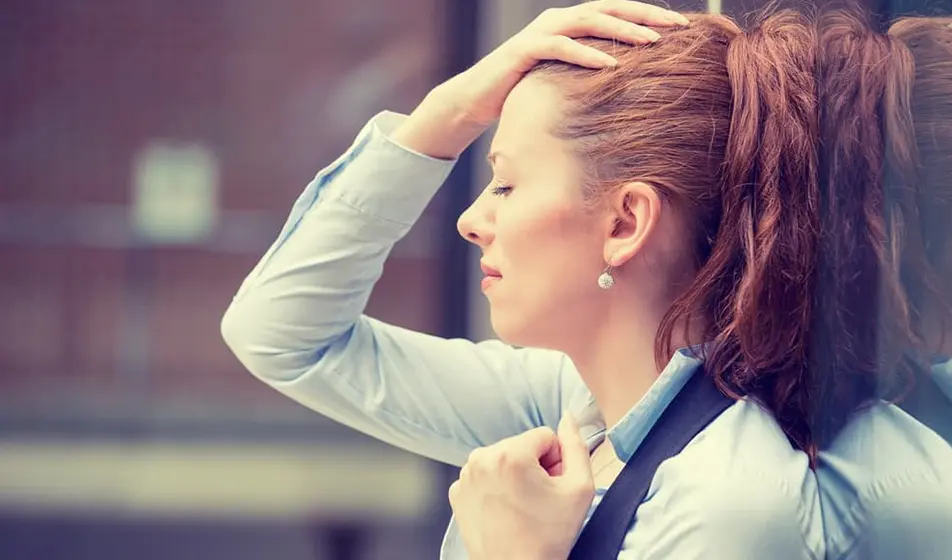 A woman has the back of her head against a window. She has a hand on her forehead and is looking very stressed.